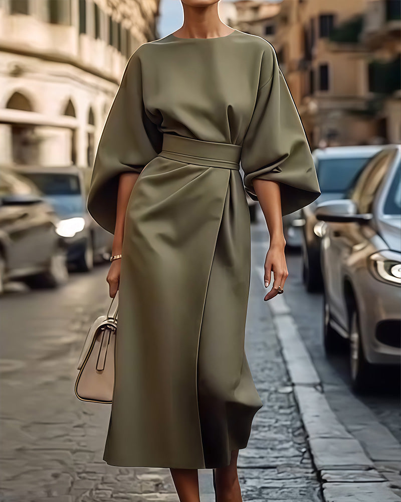 Olive green version of the belted dress with wide sleeves and a wrap-style skirt, worn with a cream handbag on a cobbled street. 2