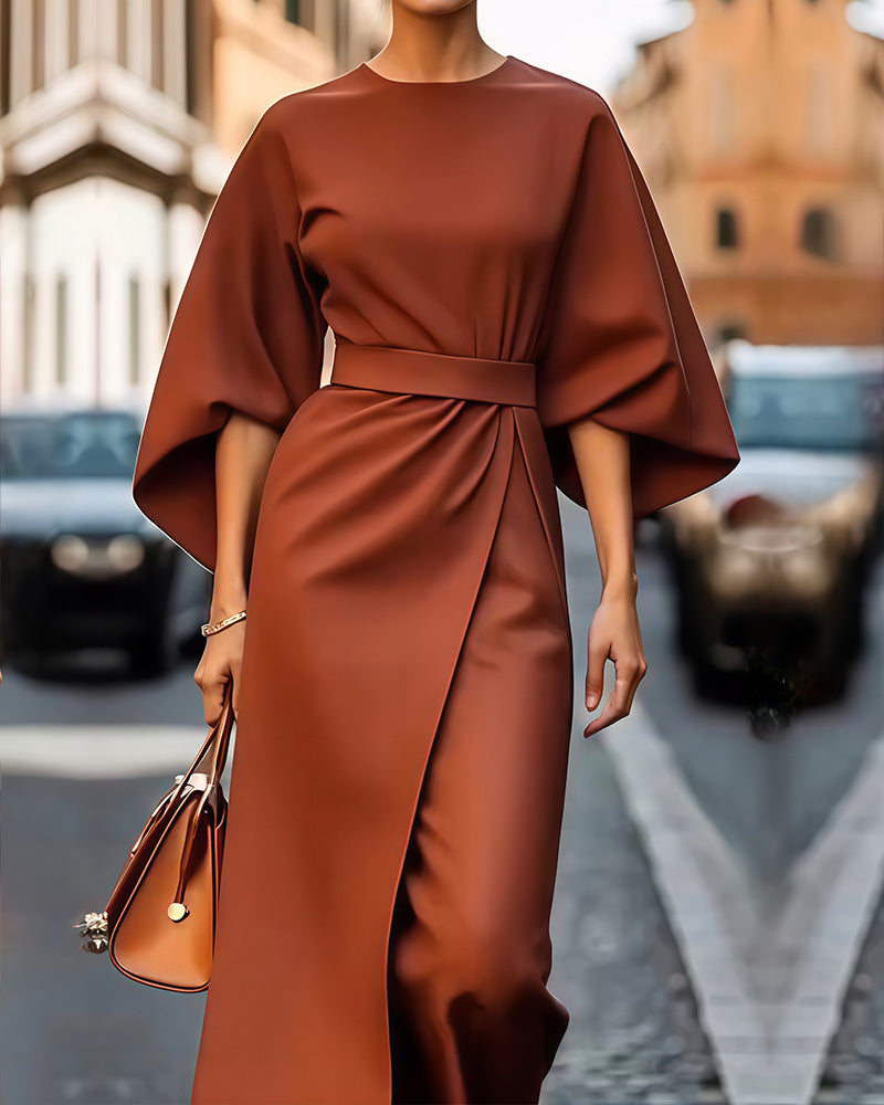 Rust-brown version of the belted dress with draped sleeves and overlapping skirt panel, shown with a tan leather handbag. 3