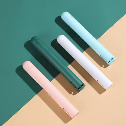 Four closed straighteners in light blue, white, dark green and pink lying diagonally on a green and peach split background. 5