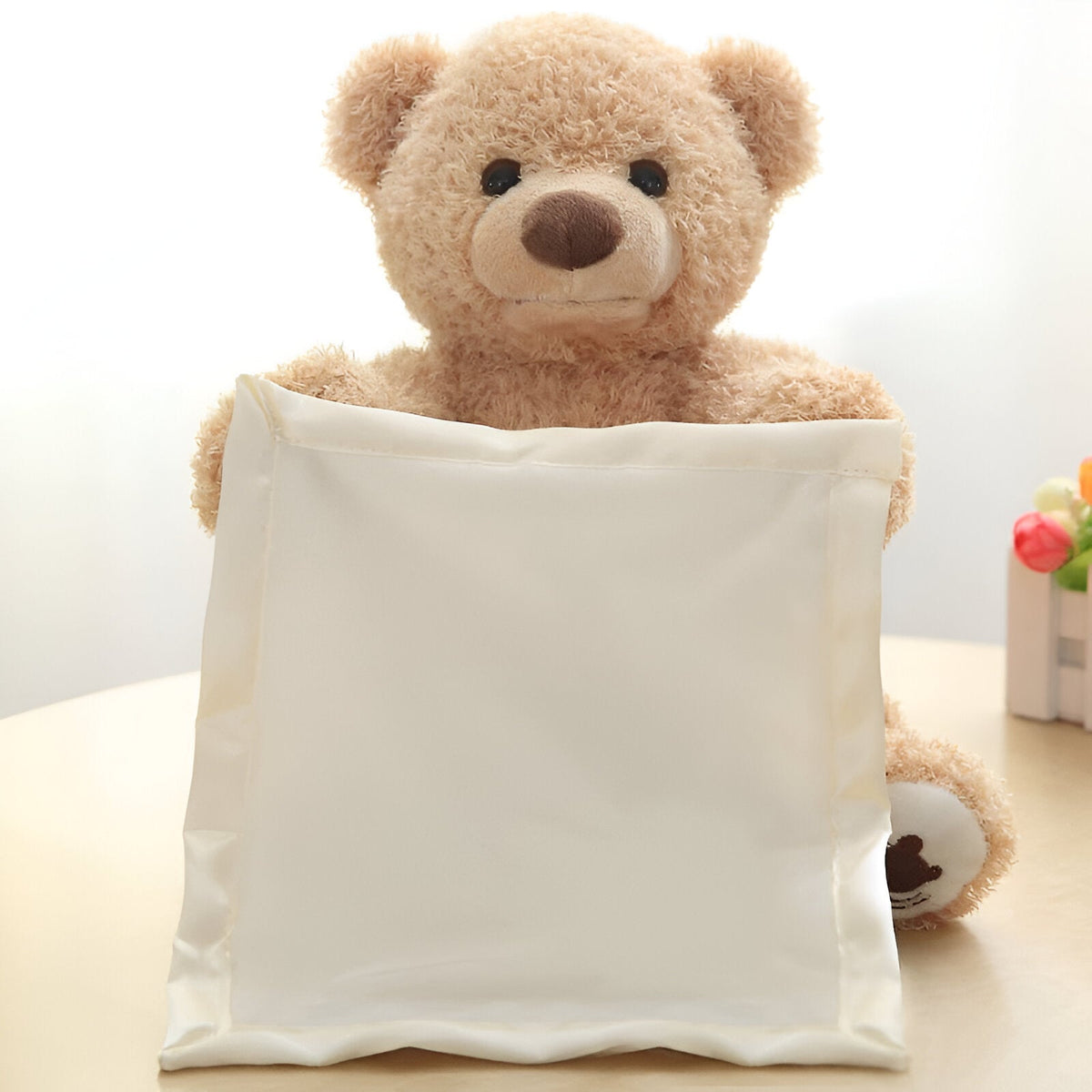 Front view of the fluffy beige teddy bear holding a cream satin cloth up in front of its body on a table. 2