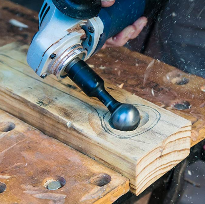 Angle grinder with a ball-shaped carving bit hollowing a marked-out recess in a plank on a workbench 2