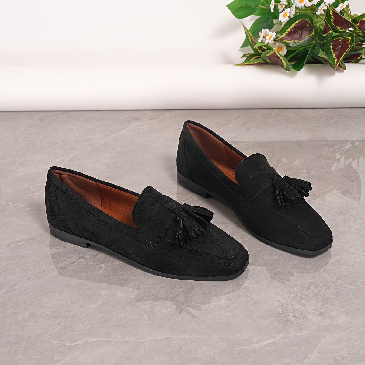 Pair of black tasselled loafers on a grey floor, showing the tan lining 25