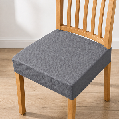 Grey honeycomb-textured seat cover fitted over the seat of a light wooden slatted chair on a wooden floor. 9