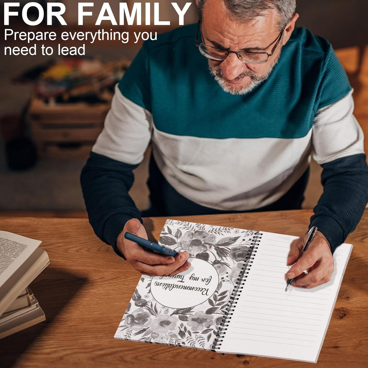 Man in glasses and a teal and white jumper holds a phone and writes with a pen in the open planner on a wooden desk. 4