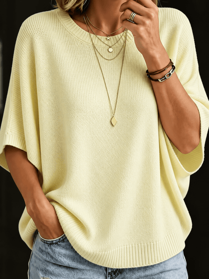 Close-up front view of the pale yellow batwing knit top with ribbed neckline and layered gold necklaces. 4