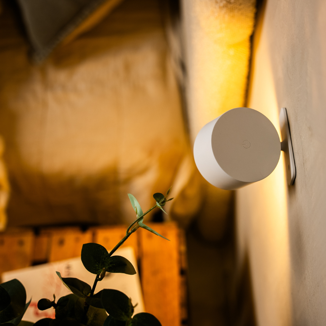 Back of the white wall light showing its flat circular end with a touch control, seen side-on against the wall. 13