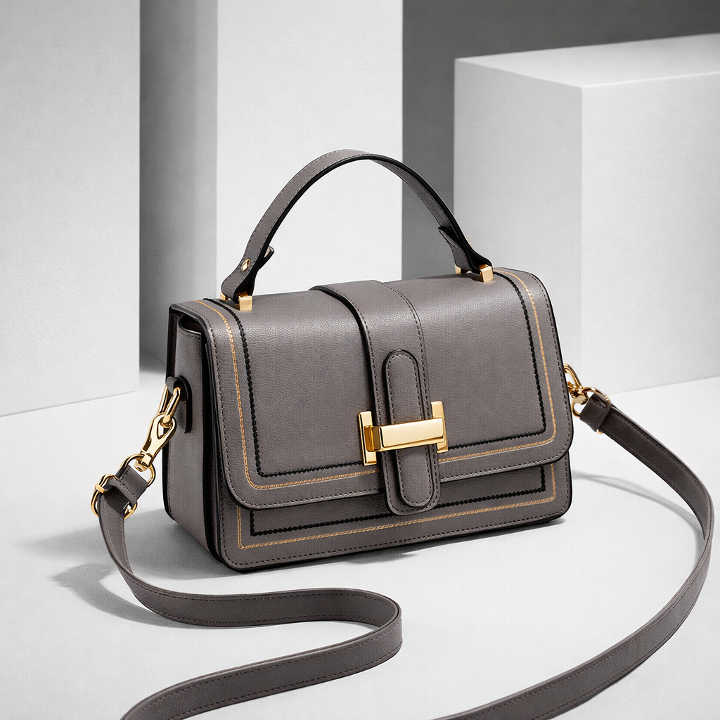 Grey version of the bag with gold clasp and stitched trim, angled view with the long strap looped across a white studio floor. 3