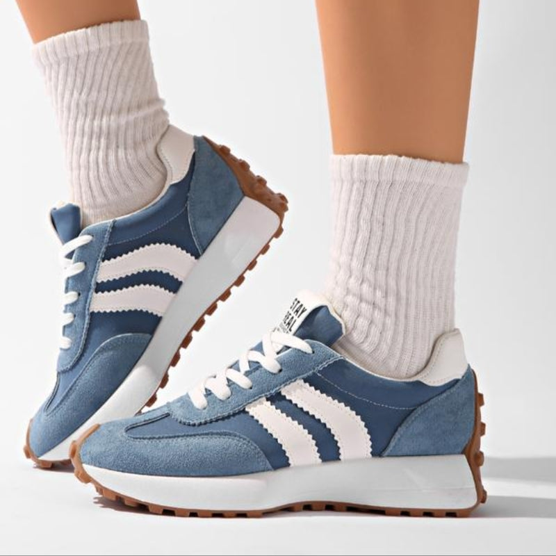 Side view of blue suede trainers with white stripes worn with chunky ribbed white socks on a model 8