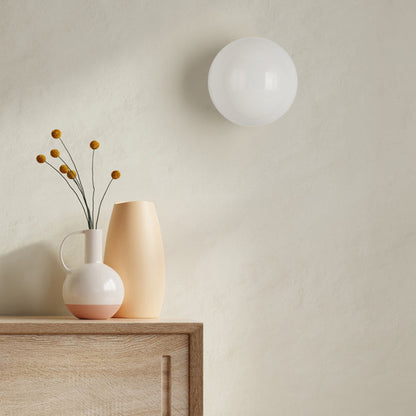 Unlit opal glass sphere on a textured cream wall above a wooden sideboard with vases 6