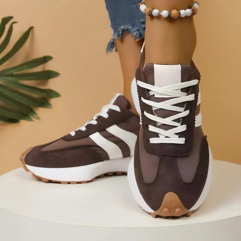 Brown trainers with white stripes and cross-laced white laces, worn on a white plinth, front view 4