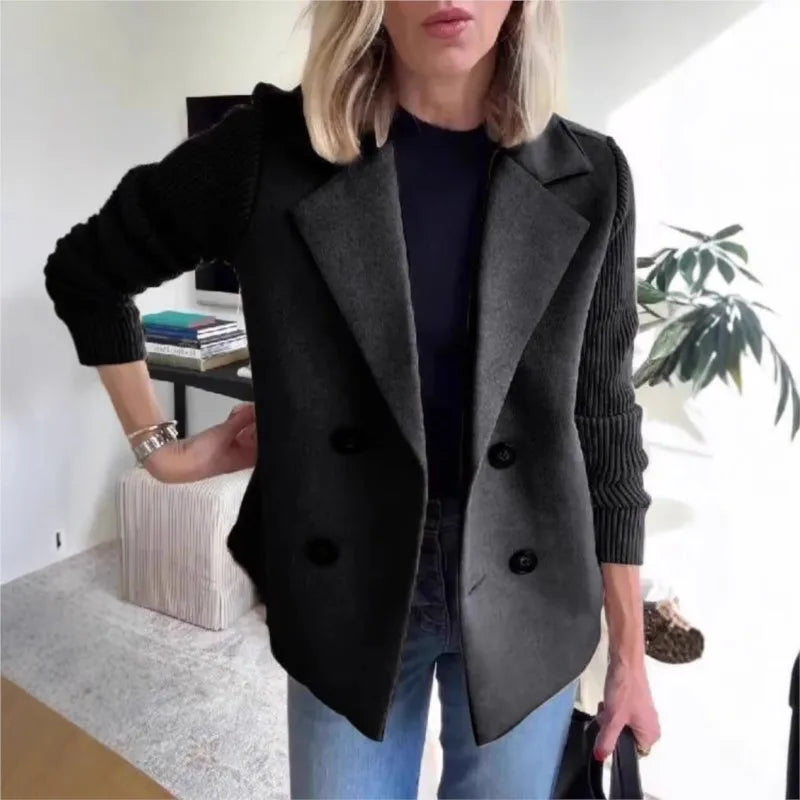Black double-breasted jacket with ribbed knit sleeves, hand on hip, worn with jeans indoors 4