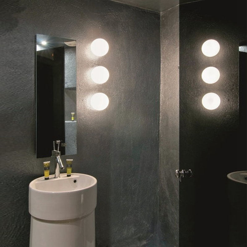 Three glowing glass spheres stacked vertically on a dark bathroom wall beside a mirror and pedestal basin 11
