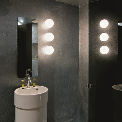 Three glowing glass spheres stacked vertically on a dark bathroom wall beside a mirror and pedestal basin 11