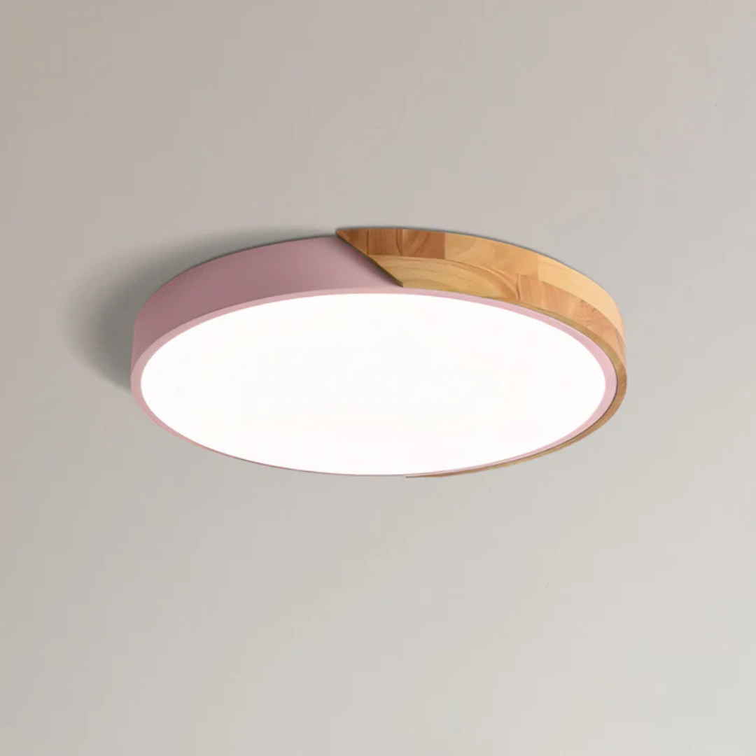 Pink and wood round ceiling light shown close up on a plain ceiling, lit 11