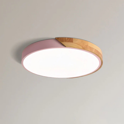 Pink and wood round ceiling light shown close up on a plain ceiling, lit 11