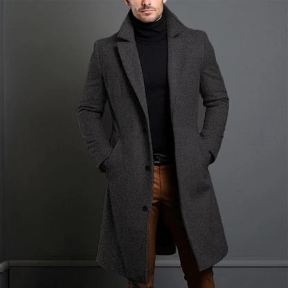 Model wearing the dark grey, textured-weave version of the longline coat, buttoned at the front over a black roll-neck. 3