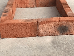 Small square of red bricks laid on a concrete floor, with a dark stain on one brick 7