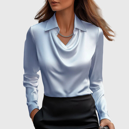 Model wearing the satin cowl-neck blouse in pale powder blue with soft draping at the neckline, worn with a black skirt. 4