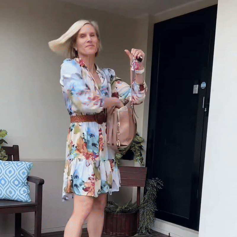 Blonde woman in a floral dress and belt tossing her smooth hair as she heads out of a front door holding her keys. 8
