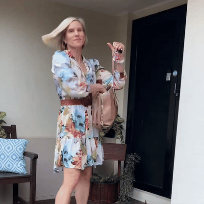 Blonde woman in a floral dress and belt tossing her smooth hair as she heads out of a front door holding her keys. 8
