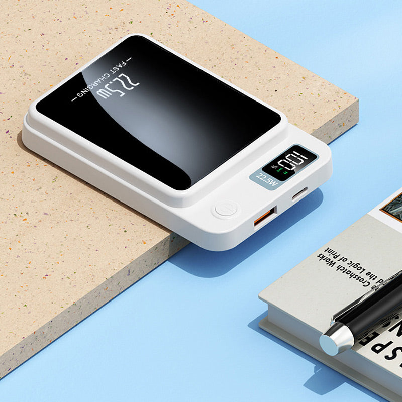 White power bank lying flat on a ledge, showing its USB-A and USB-C ports, power button and display, beside a book and pen. 6
