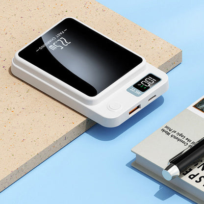 White power bank lying flat on a ledge, showing its USB-A and USB-C ports, power button and display, beside a book and pen. 6
