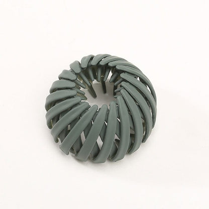 Single matte sage green spiral clip with curved overlapping slats and inner teeth, photographed against a plain background. 15