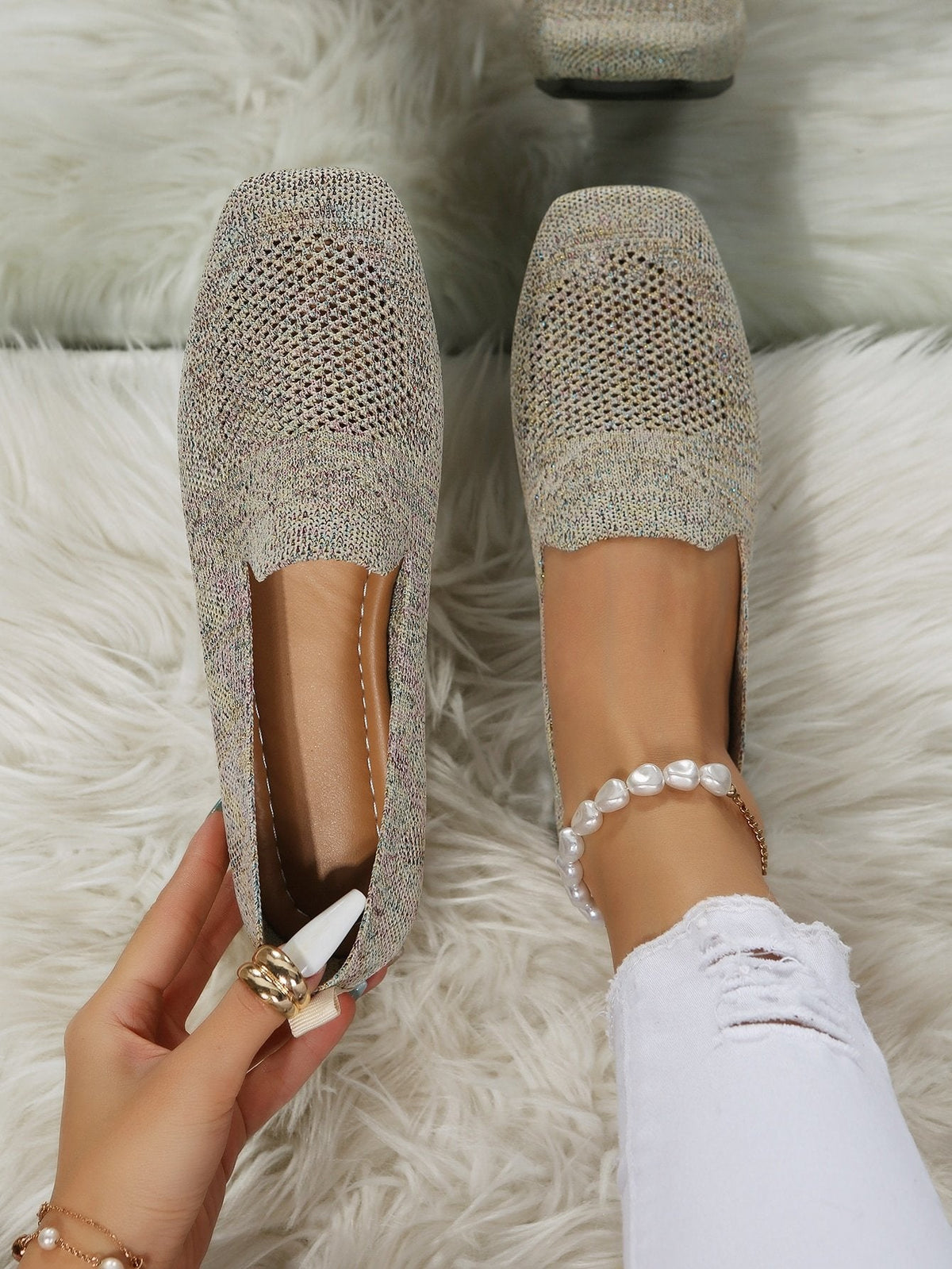 Top-down view of speckled beige knit slip-on shoes with square toes and perforated mesh, one worn and one held open to show the cushioned footbed. 21