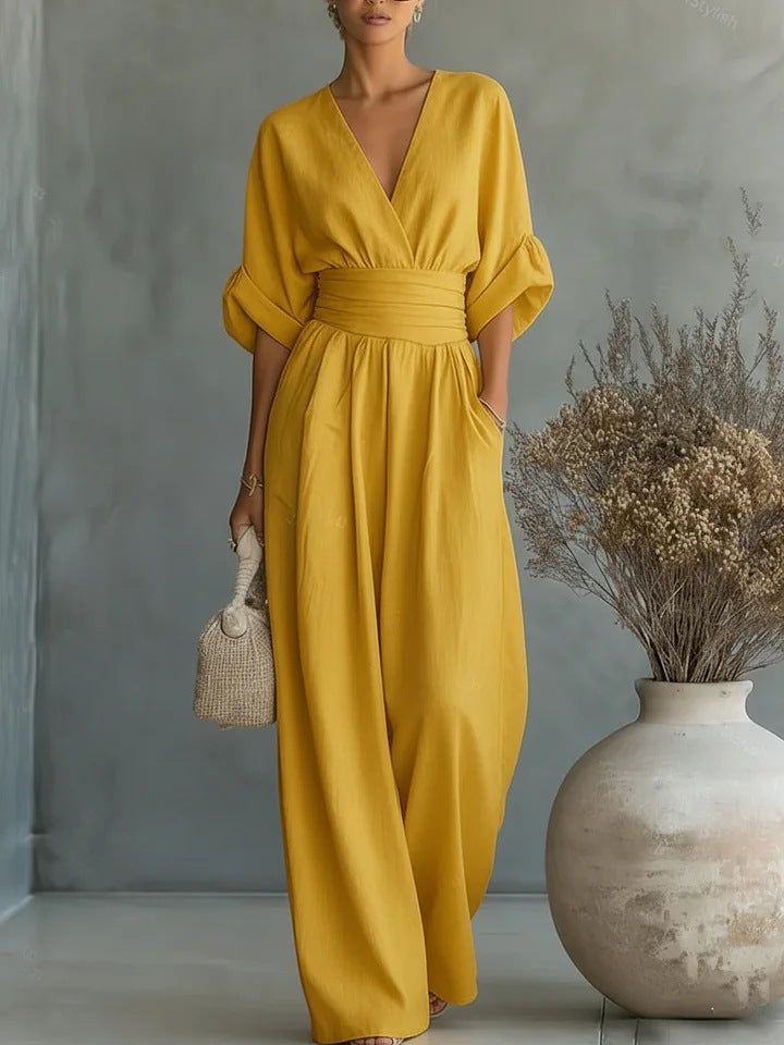 The jumpsuit in mustard yellow, shown on a model with one hand in a pocket, against a grey studio wall. 3