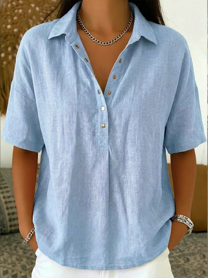 Model wearing the short-sleeved blouse in pale blue, with metal snap buttons and a chain necklace 3