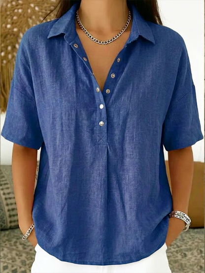 Model wearing the short-sleeved blouse in royal blue, with metal snap buttons and a chain necklace 1