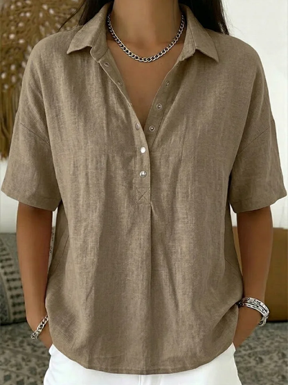 Model wearing the short-sleeved blouse in taupe, with metal snap buttons and a chain necklace 2