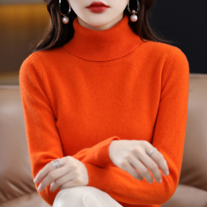 Bright orange roll-neck jumper on a seated model with relaxed hands, showing the ribbed fold-over collar and fine knit. 10
