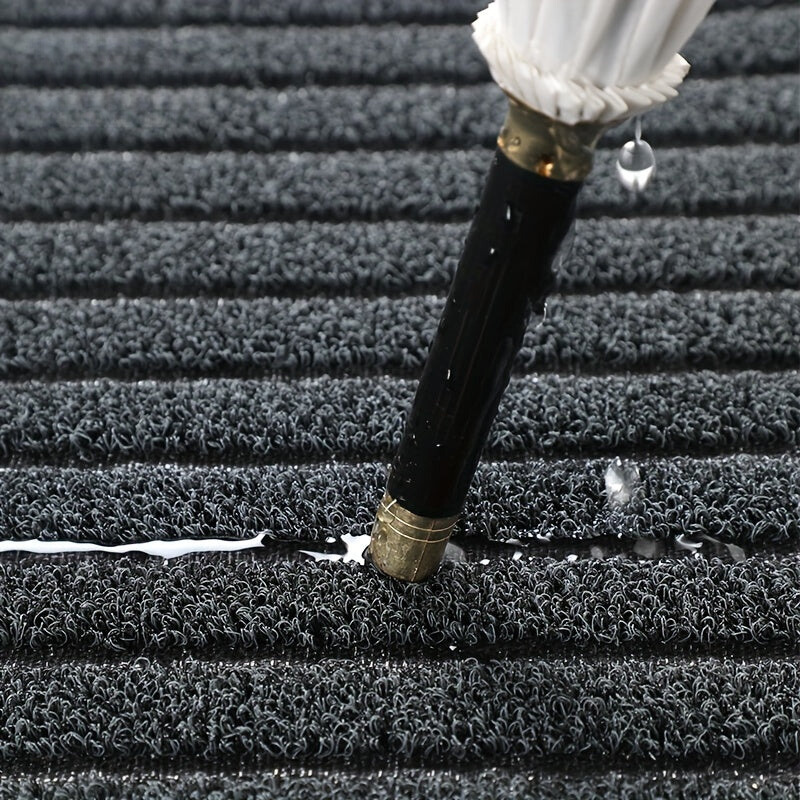 Close-up of a wet umbrella tip pressed into the grey looped pile, with water drops collecting in the grooves. 3