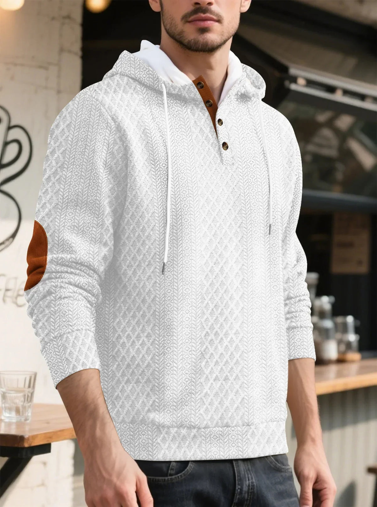 Model in a white diamond-textured hoodie in a cafe setting, three-quarter view with tan elbow patch and drawstrings 5