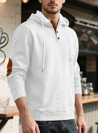 Model in a white diamond-textured hoodie in a cafe setting, three-quarter view with tan elbow patch and drawstrings 5