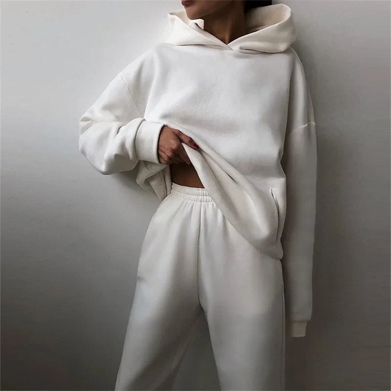 Model leaning on a wall in a white hoodie and joggers, one hand tugging the hem 5