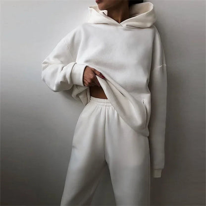 Model leaning on a wall in a white hoodie and joggers, one hand tugging the hem 5