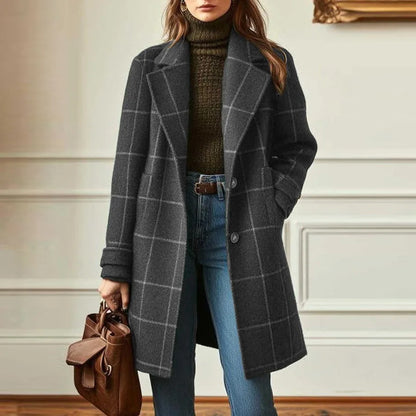 Model in a panelled room wears the charcoal checked coat with pale check lines, holding a brown bag 5
