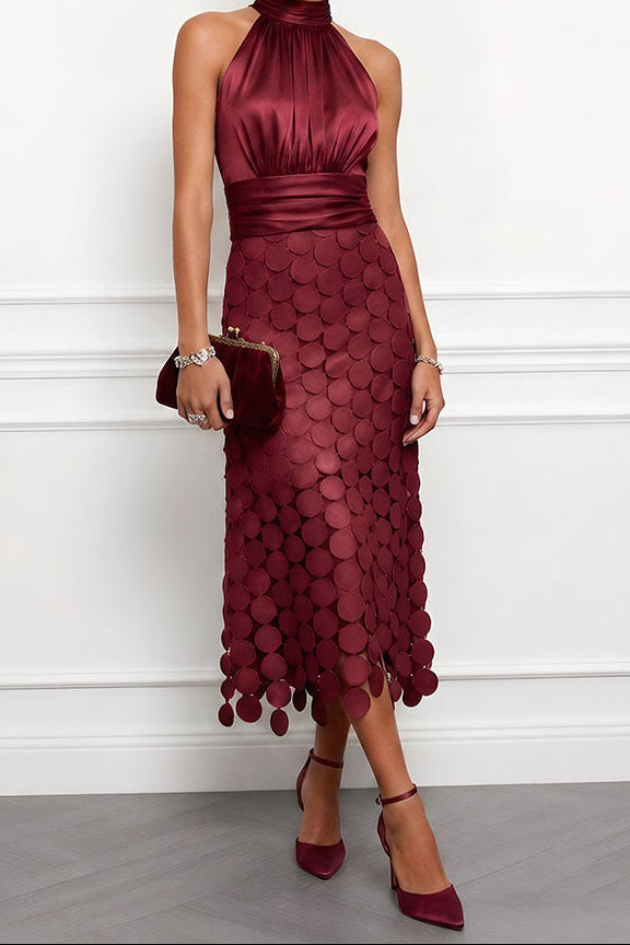 Model wears the halter midi dress in deep burgundy with a ruched satin bodice, disc appliqué skirt, small clasp clutch and heels. 5