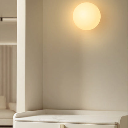 Lit opal glass sphere fixed to a cream wall above a white console with marble top 3
