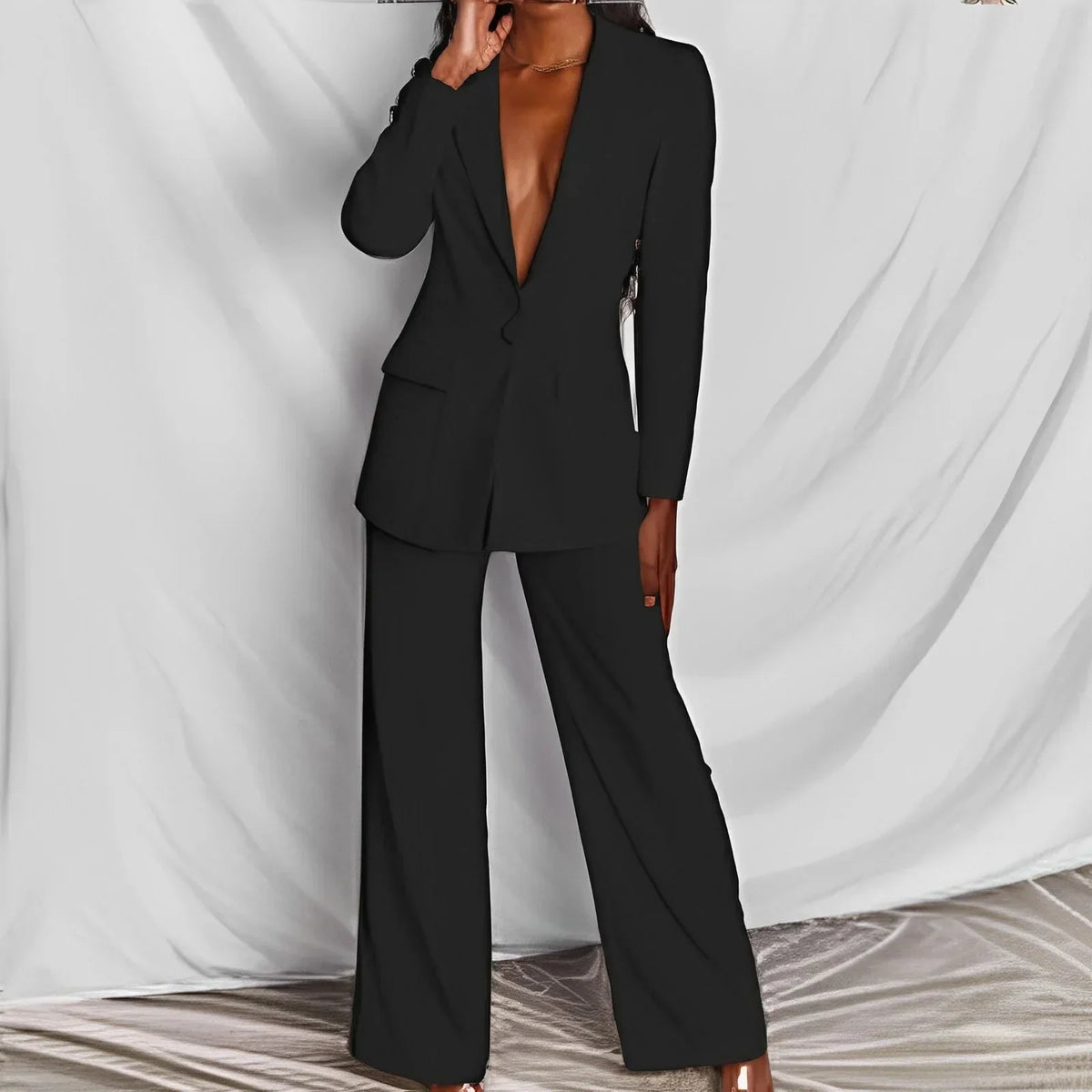 Black blazer and wide-leg trousers on a model, front view with her hand at her face against draped backdrop 5