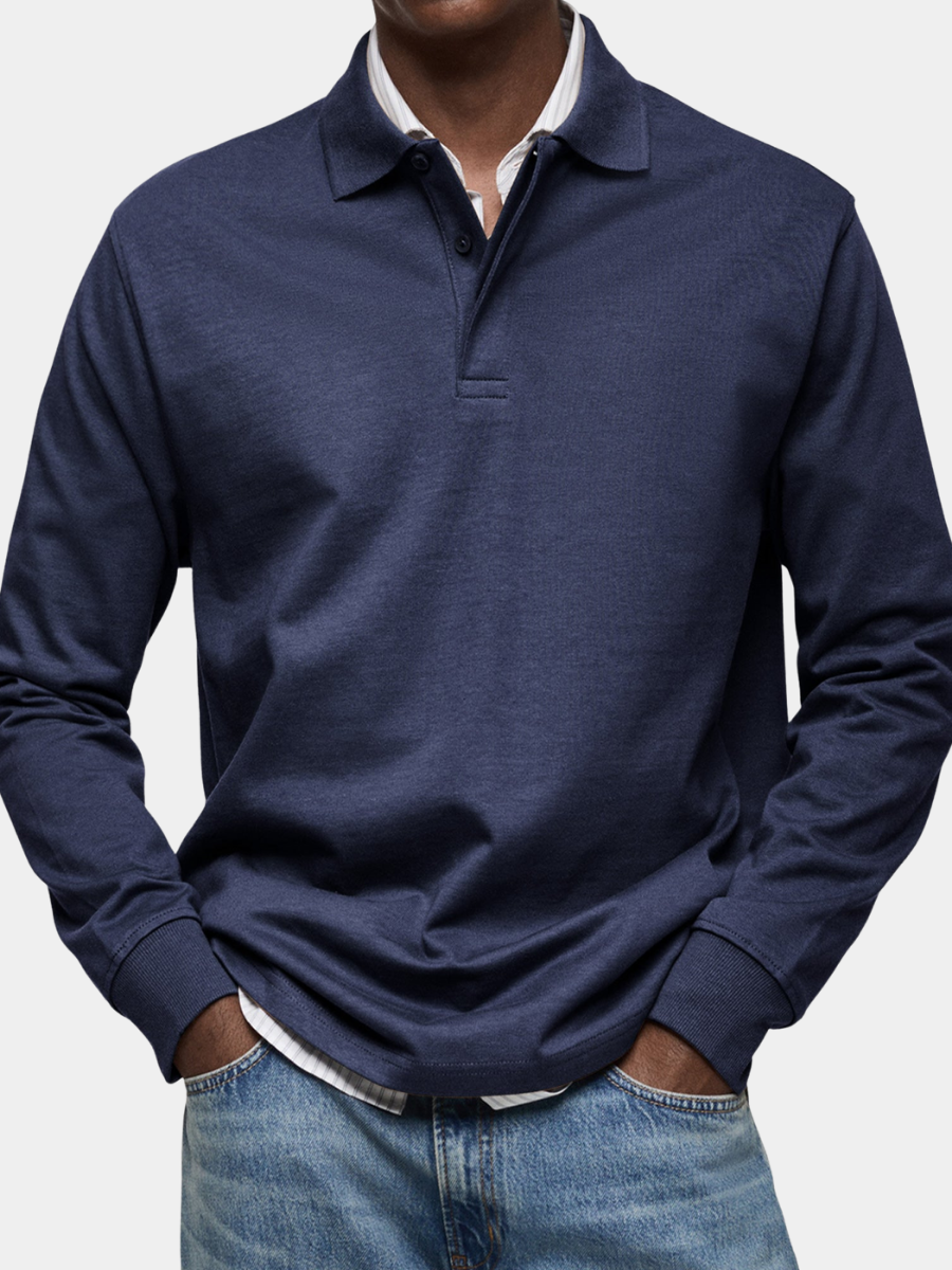 Model wearing the long sleeve polo in navy over a striped shirt, with blue jeans, in a close-cropped front view. 1