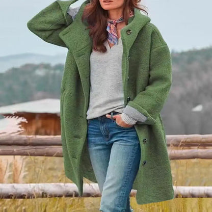 Green coat worn open over a grey top and scarf, hand in jeans pocket, outdoors by a fence 5