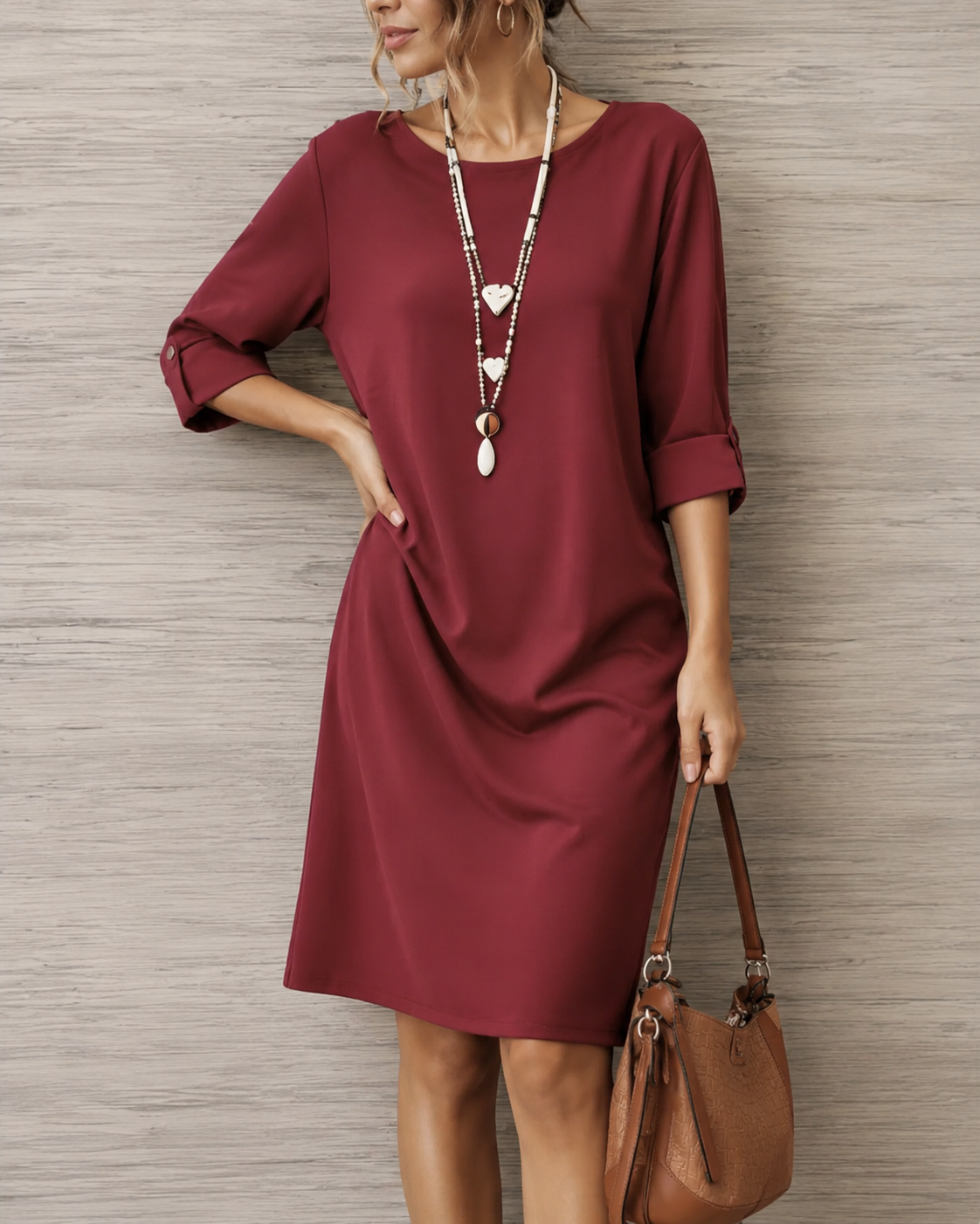 Burgundy shift dress with button sleeve tabs worn by a model with hand on hip, carrying a brown shoulder bag 6