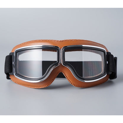 Front view of the goggles with tan stitched padding, chrome-trimmed frame, clear lenses and a black elastic strap. 7