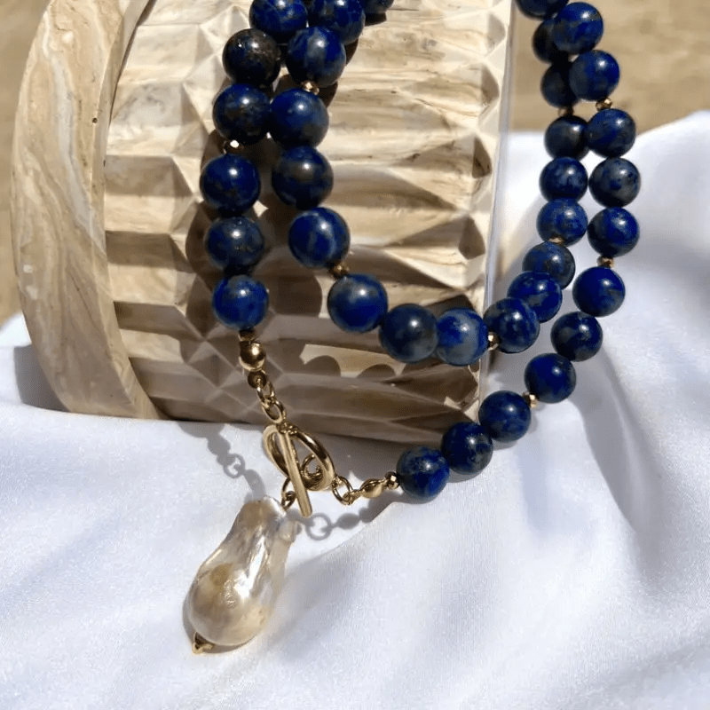 Double loop of blue beads hanging over a carved wooden piece, pearl dangling at the toggle 7