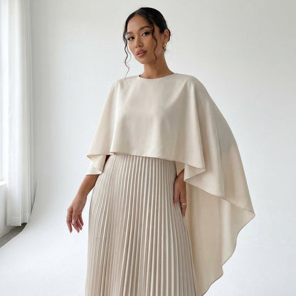 Close-up of the cream dress on a model, showing the round neckline, flowing cape and pleated skirt 2