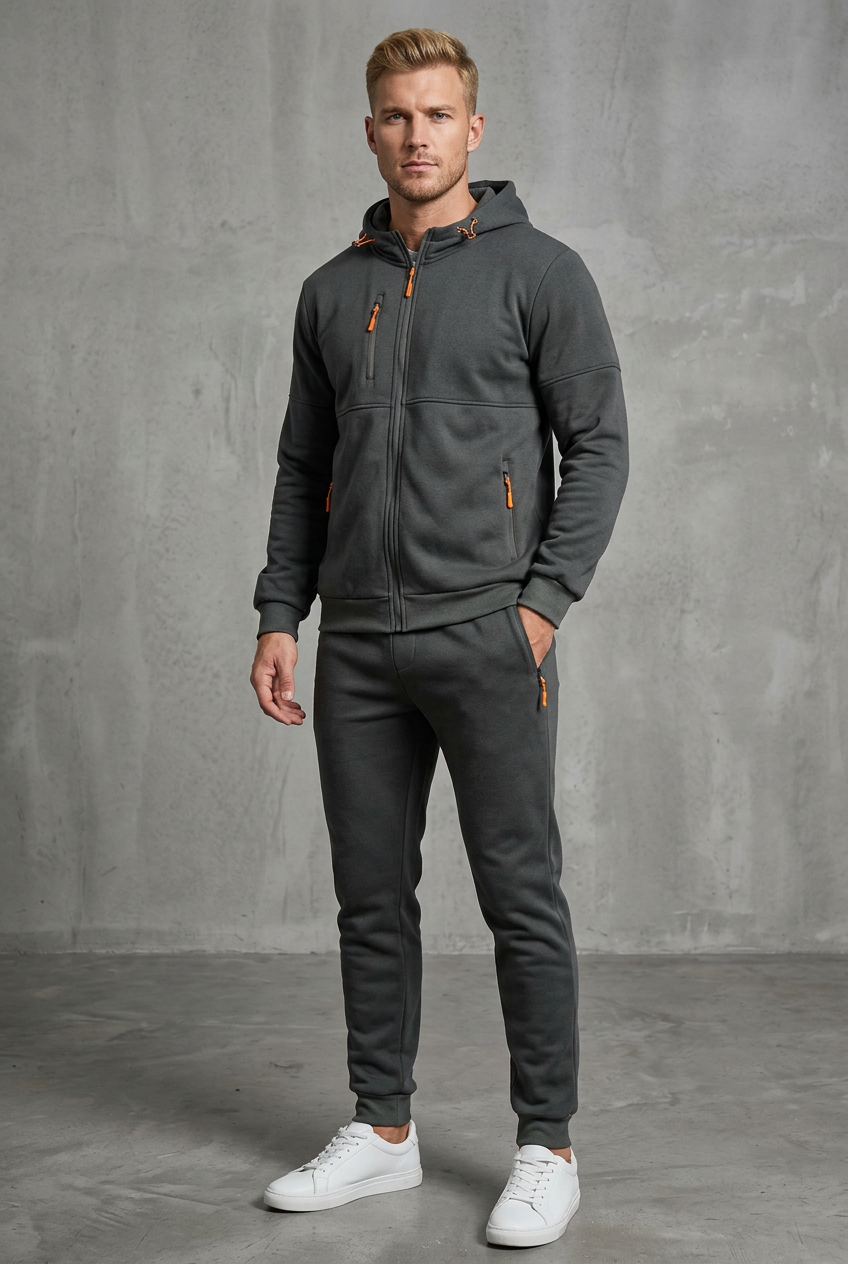 Man in dark grey hooded tracksuit with orange zip pulls, one hand in trouser pocket 4