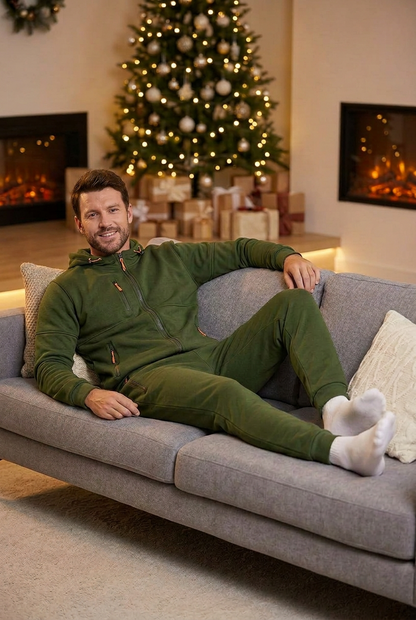 Smiling man in an olive green hooded zip set relaxing on a grey sofa by a Christmas tree 1